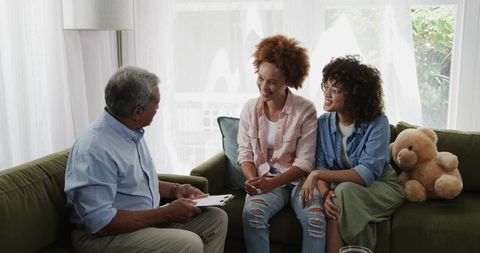 Multigenerational African American family talking with senior holding clipboard on sofa