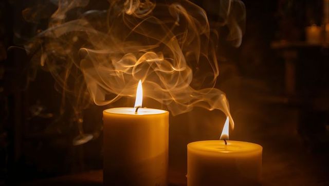 Two burning pillar candles emitting warm amber glow with swirling smoke