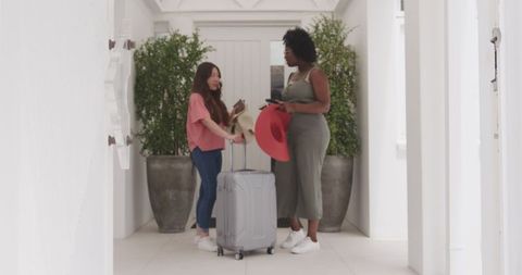 Two friends arriving at white hotel interior with suitcases