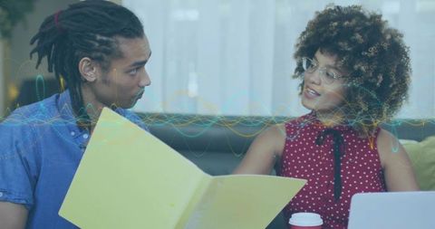 Discussing project with yellow folder and laptop in casual lounge, collaborative teamwork