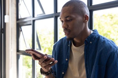 African American man using smartphone by industrial window in casual coworking office
