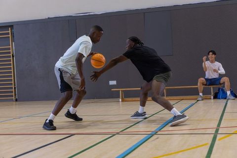 Diverse friends playing basketball indoors dribbling and defending on gym court spectator
