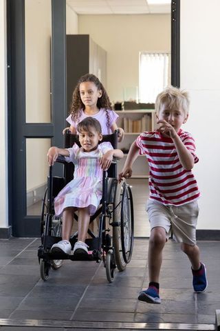 Diverse children playing in school corridor, girl sitting in wheelchair, boy running