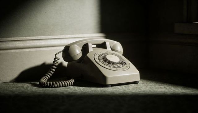 Vintage beige rotary telephone in sunlit corner casting dramatic shadow on green carpet