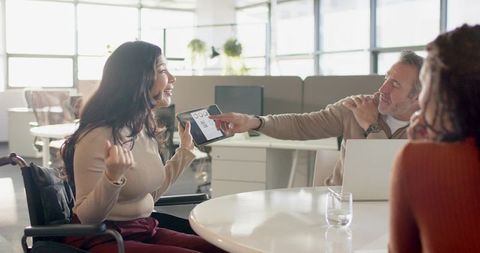 Collaborating team with woman in wheelchair presenting tablet at modern office round table