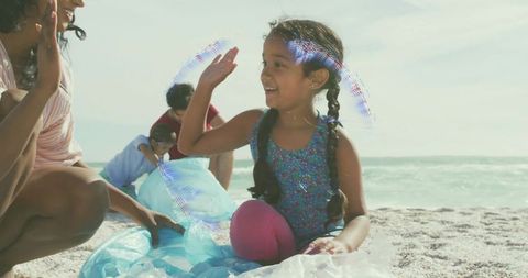 Smiling girl giving high five on sunlit beach with family, bubbles and mermaid play