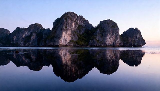 Limestone karst islands reflecting in glassy twilight water, serene coastal landscape