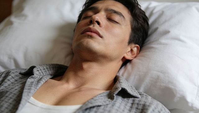 Young man resting peacefully on pillow wearing gray checked shirt and white undershirt