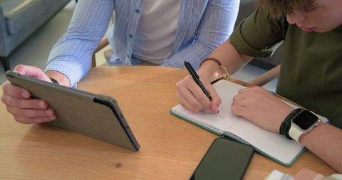 Teenager Taking Notes While Adult Guiding on Tablet During Home Study Session
