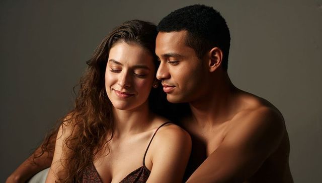 Intimate embracing couple leaning close with soft light, warm skin tones, gray backdrop
