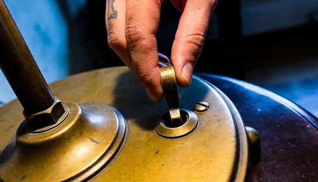 Right hand turning vintage brass lamp key on patinated base close-up warm moody light