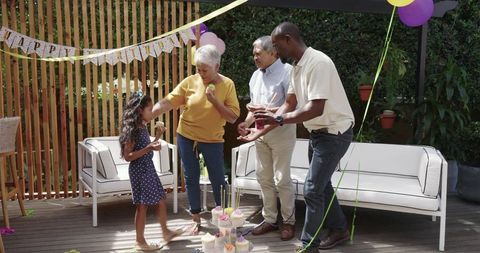 Diverse multigenerational family celebrating birthday on sunny backyard deck with cupcakes