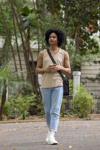African american man walking on tree-lined sidewalk wearing casual top and crossbody bag