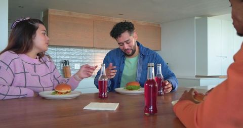 Friends enjoying casual burger lunch at modern kitchen island with red soda bottles