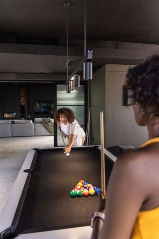 Diverse women playing pool in modern game room with black felt table and pendant lights