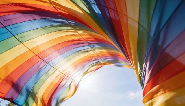 Billowing rainbow flag forming arched tunnel under blue sky with sun flare