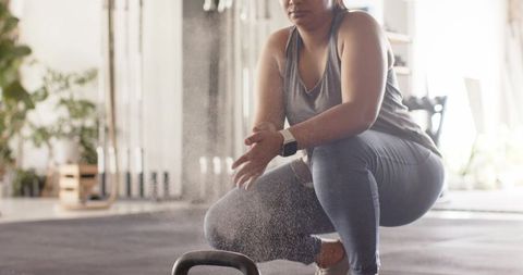 African american woman clapping hands creating chalk dust before kettlebell workout