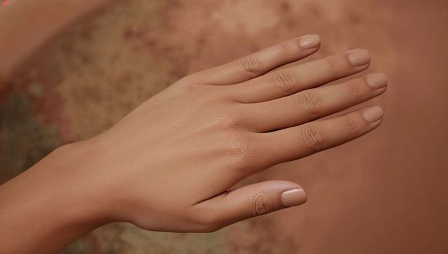 Right hand resting on warm terracotta with neutral manicure and smooth skin closeup