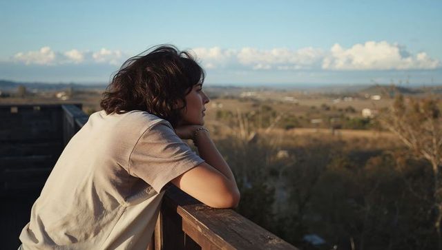 Young woman leaning on wooden balcony gazing over expansive rural valley at sunset