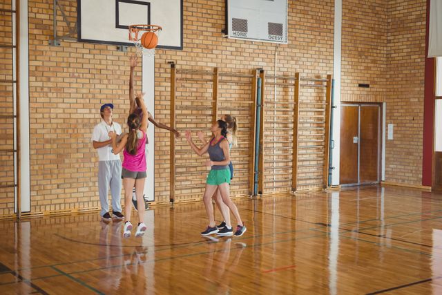 High school students playing basketball in a gymnasium, with one team defending against the other. Ideal for use in educational materials, sports promotions, fitness campaigns, and youth activity advertisements.
