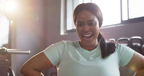 Laughing african american woman working out in gym wearing mint top, backlit energy