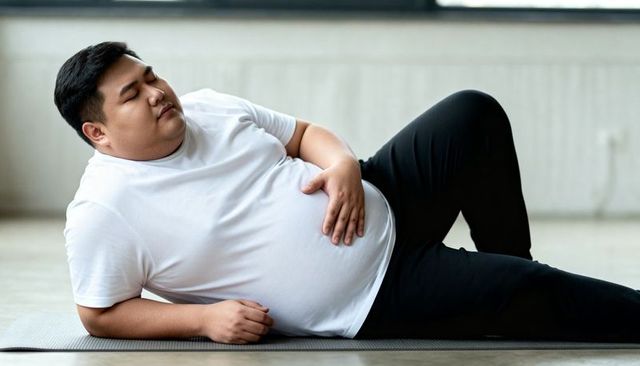 Plus-size man resting on yoga mat in bright minimalist gym after low-impact workout