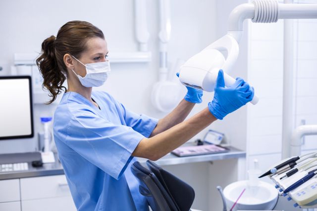 Dental assistant adjusting light in modern dental clinic. Ideal for use in healthcare industry publications, dental clinic brochures, websites for dental services, and marketing materials showing professional dental care environments.