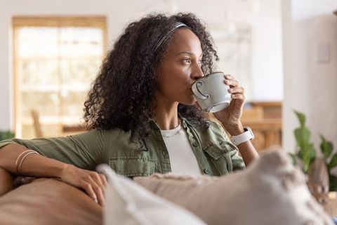 African american woman sipping coffee while relaxing on couch with cozy pillows and mug