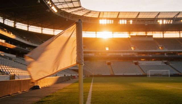 White corner flag fluttering at sunset on empty football stadium pitch with lens flare
