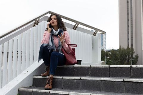 Urban commuter taking phone call on overpass stairs with tote bag and takeaway coffee