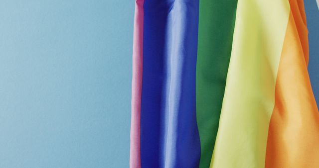 Bright rainbow-colored drapes of fabric hanging against a blue background. Useful for themes related to diversity, LGBTQ+, fashion, interior design, and artistic expressions. Could be used in advertisements, promotional materials, or web design to add a pop of color and showcase inclusion and creativity.