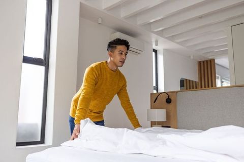 Man making bed in modern minimalist bedroom with white linens