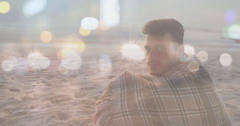 Man Wrapped in Plaid Blanket on Beach with Nighttime Bokeh