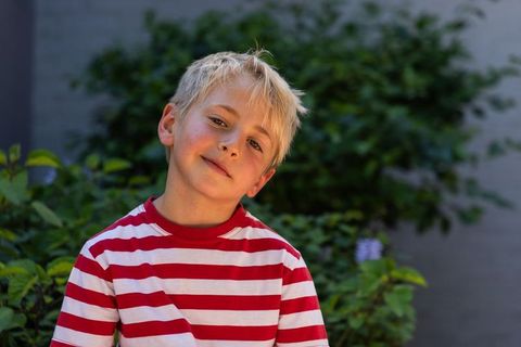 Relaxed preteen boy in red-and-white striped shirt in green garden, natural light portrait