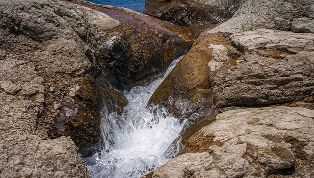 Churning seawater flowing through narrow rocky channel with polished bedrock texture