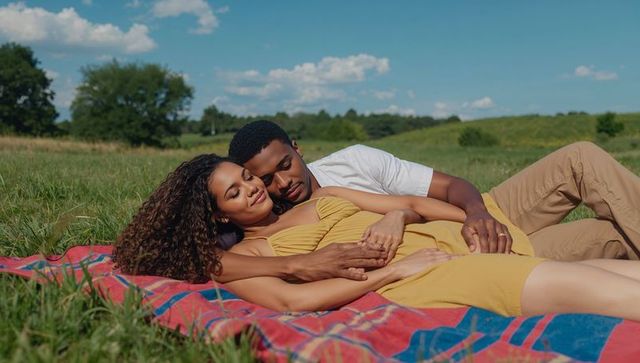 Couple cuddling on blanket in sunlit meadow enjoying summer romance and relaxation