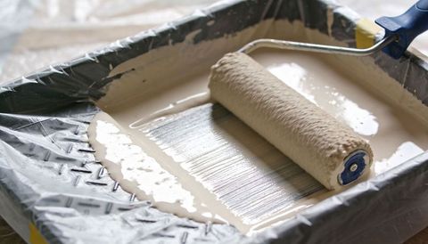Paint roller spreading creamy beige paint in lined tray, textured roller close-up