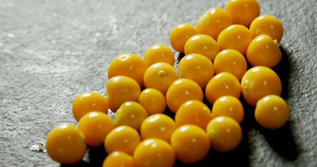 Yellow cherry tomatoes laying in an irregular arrangement on a black stone surface, catching natural light. Perfect for use in culinary blogs, healthy eating promotions, supermarket displays, or nutritional articles. Highlights the freshness and vibrant color of the produce.