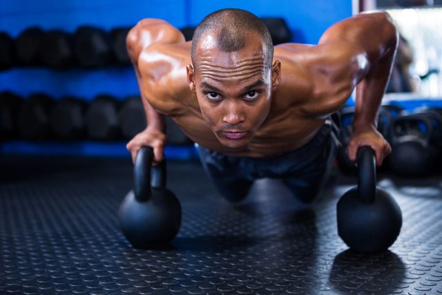 This image is ideal for fitness blogs, workout programs, gym advertisements, and health-related articles. It showcases a strong, determined man performing push-ups with kettlebells, emphasizing strength and dedication.