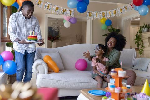 African american family celebrating birthday at home carrying cake, balloons, cupcakes