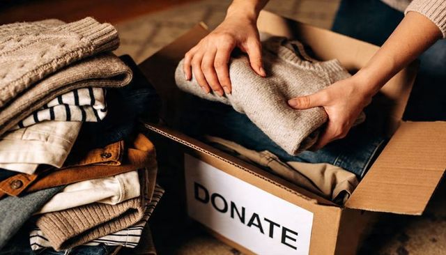 Woman packing cozy sweaters into donate box for charity, sustainable wardrobe declutter