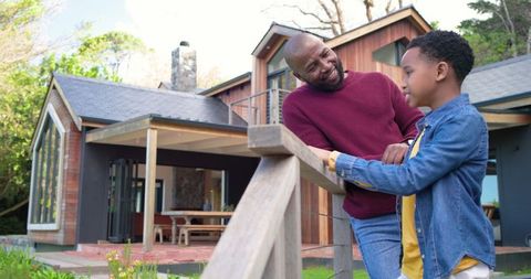 African american father and son sharing conversation on porch railing of modern wood home