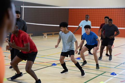 Diverse male athletes training agility drills on indoor volleyball court with coach
