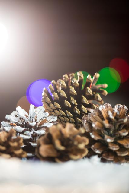 Close-up of pine cone decoration on fake snow with colorful festive lights in the background. Ideal for holiday greeting cards, seasonal advertisements, winter-themed designs, and Christmas decor inspiration.
