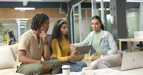 Diverse team collaborating over tablet and laptop, reviewing charts in modern coworking lounge