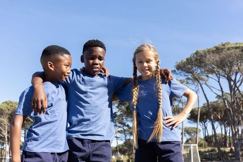 Multiracial kids standing on soccer field in blue shirts showing team spirit