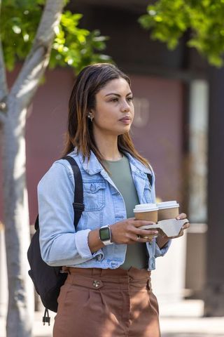 African american commuter holding two to-go coffees on sunny urban sidewalk, denim jacket