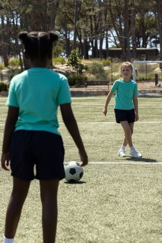 Girls practicing soccer on turf field during youth training session with ball and teamwork