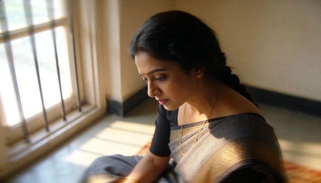 Contemplative indian woman in dark grey saree with gold border sitting by barred window