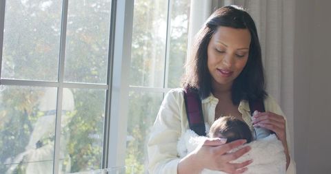 Asian mother holding baby by window in sunlit room